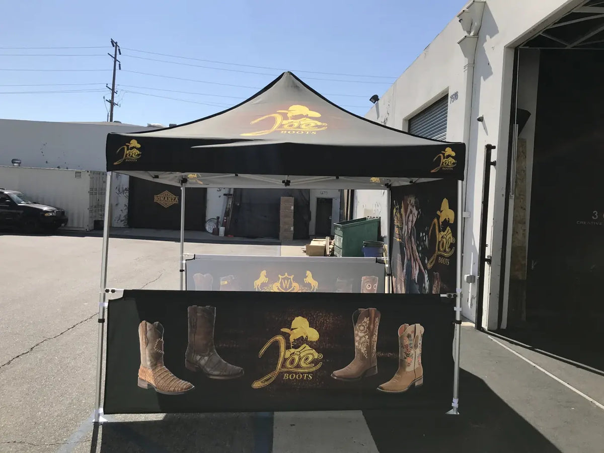 Front view of a black custom printed canopy with a printed half wall showing boots and a gold logo