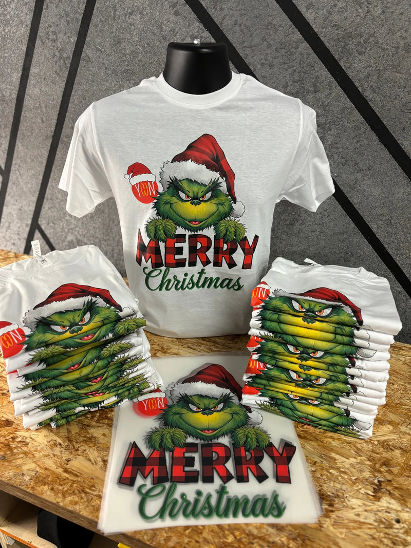 White Merry Christmas t-shirt on a display form with folded matching shirts and the full color DTF transfer sheet used to press them
