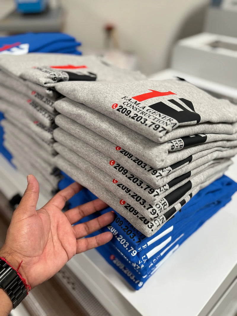 Stack of grey and blue company t-shirts printed with a construction business logo and phone number