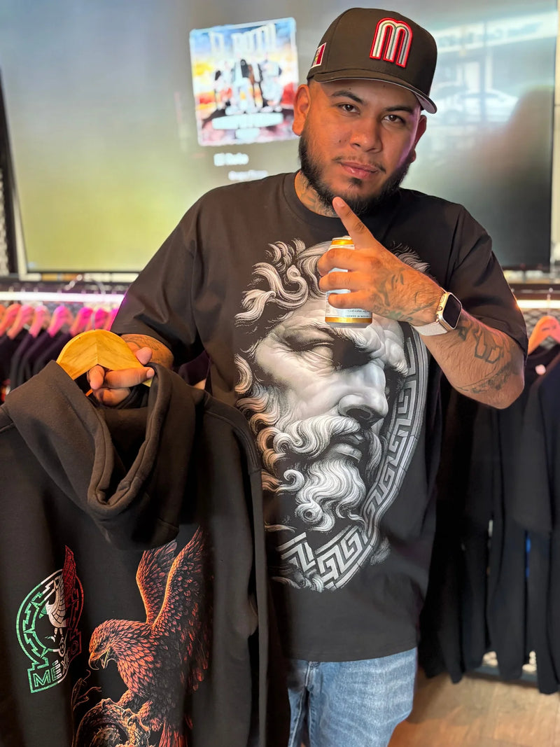 Man wearing a brown t-shirt with a full color Greek statue print and holding a matching hoodie with a full color eagle design